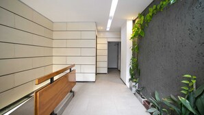 Un couloir avec un banc en bois, des murs carrelés et un mur en béton orné de plantes.
