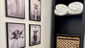 A wall with four framed pictures of a bull, a black shelf with woven baskets, and two white towels.