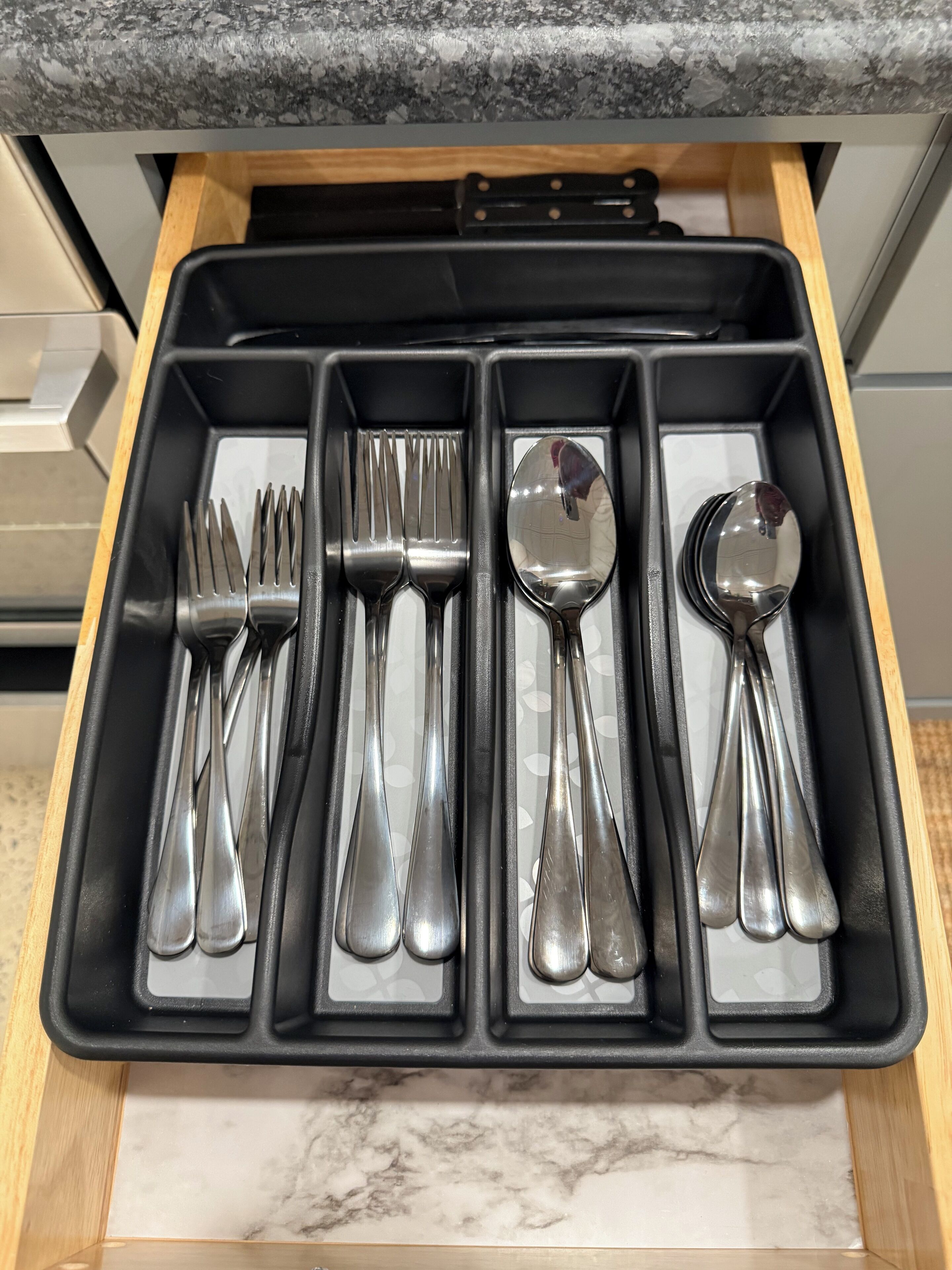 A drawer with a black interior containing various silverware items.