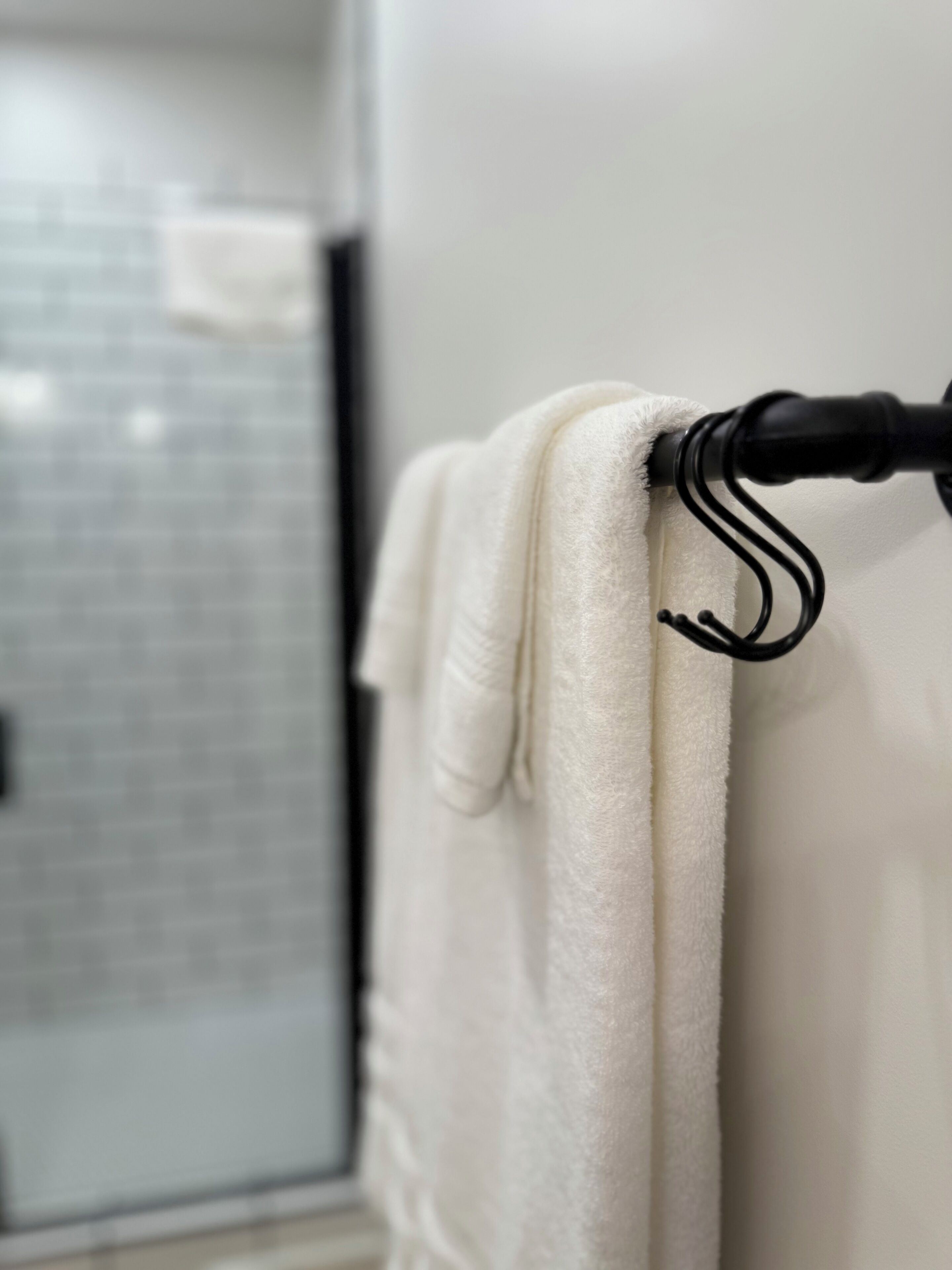 Una toalla blanca colgada en un toallero negro en un baño con pared de azulejos y puerta de ducha de vidrio al fondo.