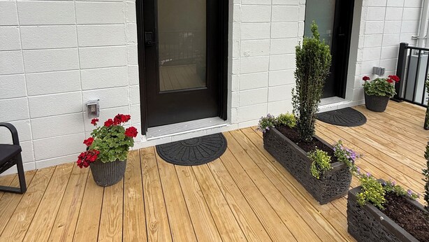 A modern building with a black door and windows, a wooden deck, and potted plants.