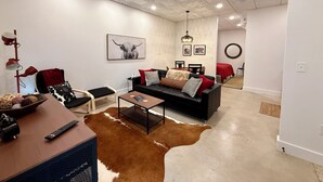 A modern living room with a cowhide rug, a black sofa with red and white cushions, a dining area with a red tablecloth, and a ceiling with recessed lighting.