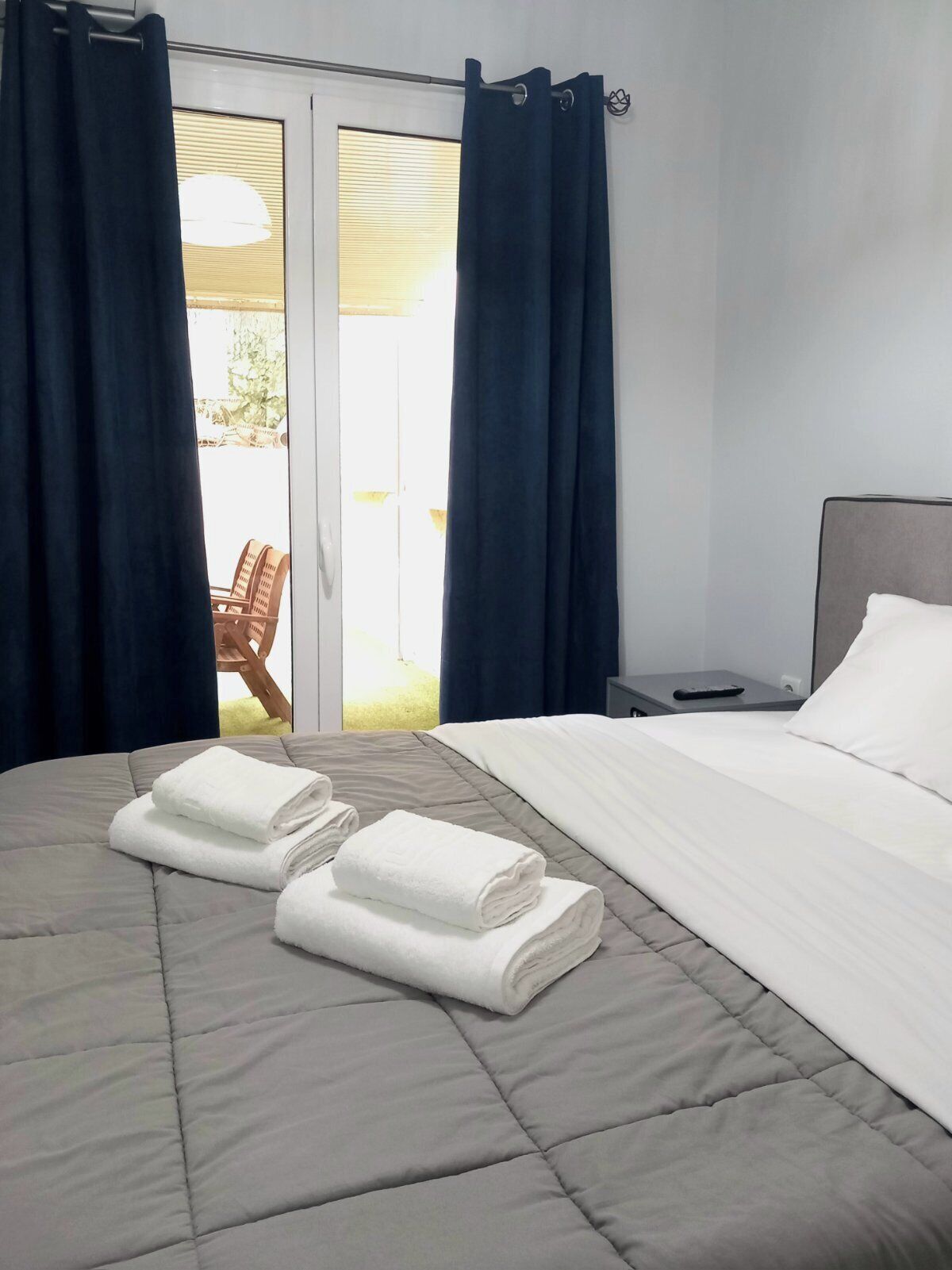 Habitación de hotel con cama, dos toallas enrolladas, mesita de noche y vistas al exterior.