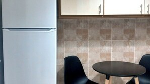 A compact kitchen with a white refrigerator, two black chairs, a small round table, and wooden cabinets above the tiled backsplash. - Petralona Antistratou Athens (Athens)