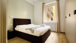 A modern bedroom with a large bed, a nightstand, a window with curtains, and a view of a building outside.