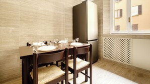 A dining area with a table set for four, a refrigerator, and a window with a view of buildings.