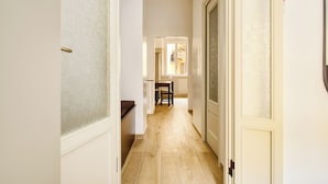 A narrow hallway with a wooden floor, a dining area with a table and chairs, and a door with a frosted glass panel.