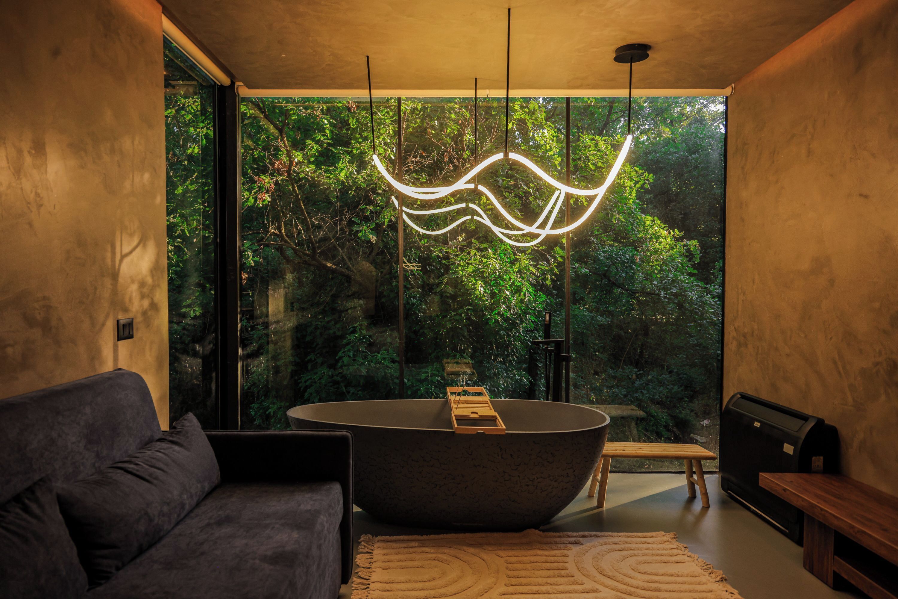 A modern interior with a large window, a dark bathtub, a sofa, and a wooden bench.