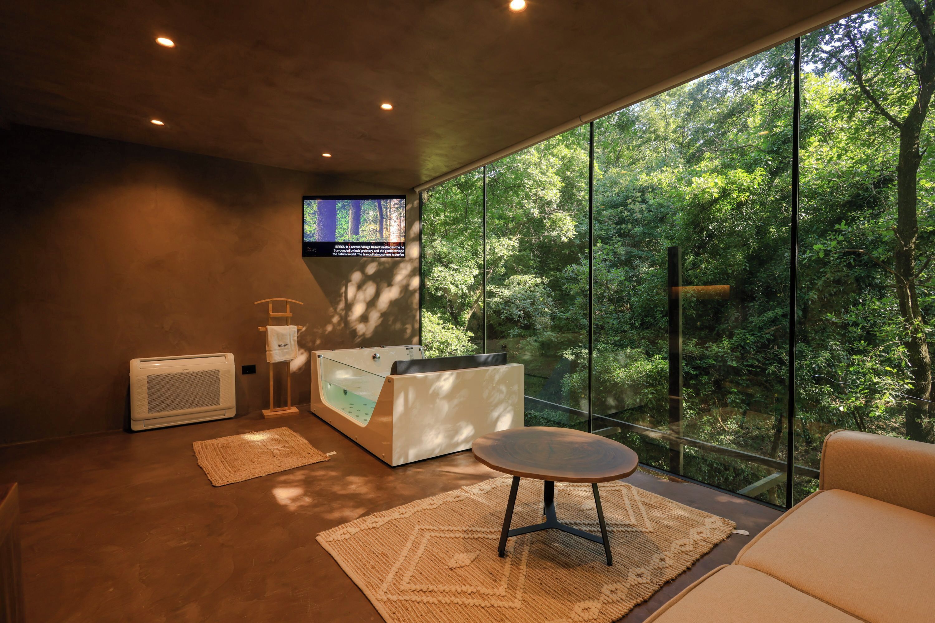 A modern room with a large window, a massage table, a massage chair, and a small table.