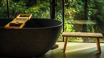 Un grand saladier noir, posé sur un plateau en bois, se trouve sur une table, à côté d’un tabouret en bois. Une fenêtre offre une vue sur la verdure.