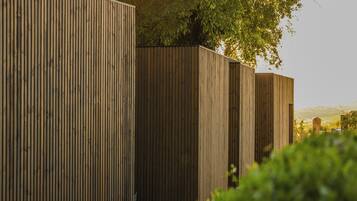 A row of vertical wooden fences with a tree and greenery in the background.