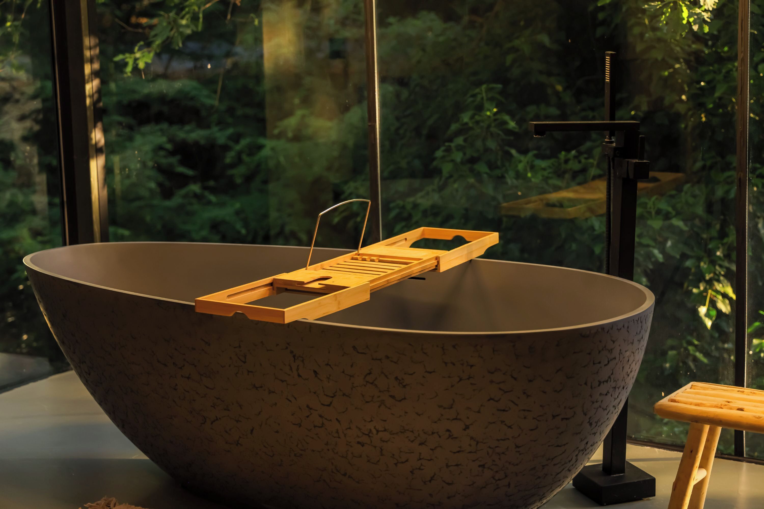 Un lavabo di grandi dimensioni a forma di conca, con un vassoio in legno, posto vicino a una finestra con vista su piante.