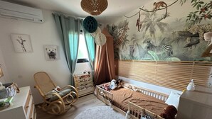 Et børneværelse med tremmeseng, gyngestol, skrivebord og et vægmaleri af jungle dyr.