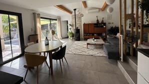 En moderne stue med spiseplads, en sofa, et sofabord og en bogreol.