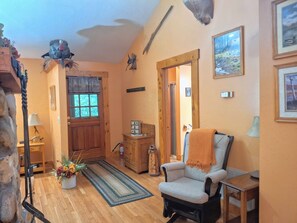 A cozy living room with a wooden floor, a comfortable armchair, a wooden cabinet, and a door leading to another room.