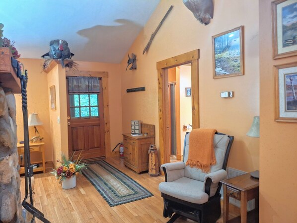Un salón acogedor con piso de madera, un sillón cómodo, un mueble de madera y una puerta que da a otra habitación.