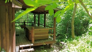 Una cabaña de madera con un banco y una mesa, rodeada de exuberante vegetación.