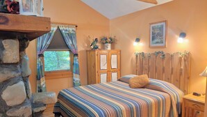 Un dormitorio acogedor con una pared de piedra, una cama con colcha a rayas, un aparador de madera y una ventana con cortinas.