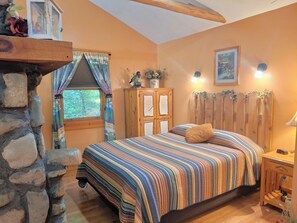 A cozy bedroom with a stone wall, a bed with a striped bedspread, a wooden cabinet, and a window with curtains.