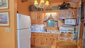 Una pequeña cocina con armarios de madera, un refrigerador, un microondas, un lavamanos y una mesa de comedor de madera con sillas.