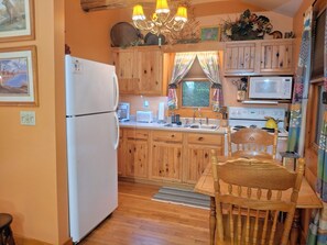 A small kitchen with wooden cabinets, a refrigerator, a microwave, a sink, and a wooden dining table with chairs.