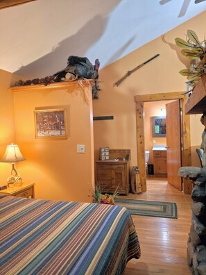 A cozy bedroom with a bed, a nightstand, a lamp, a framed picture, and a wooden dresser.