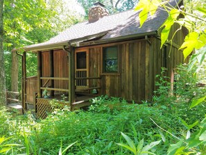 A rustic wooden cabin with a porch, surrounded by dense greenery.