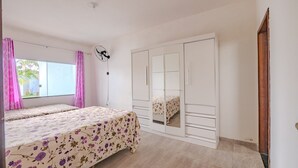 A bedroom with two beds, a wardrobe, a ceiling fan, and a window with curtains.