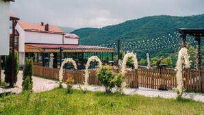 A restaurant with outdoor seating, a wooden fence, and a mountainous backdrop. - Motives Inn Dilijan (Dilijan)