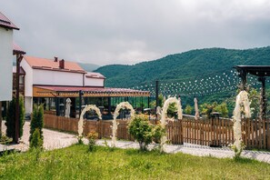 A restaurant with outdoor seating, a wooden fence, and a mountainous backdrop. - Motives Inn Dilijan (Dilijan)