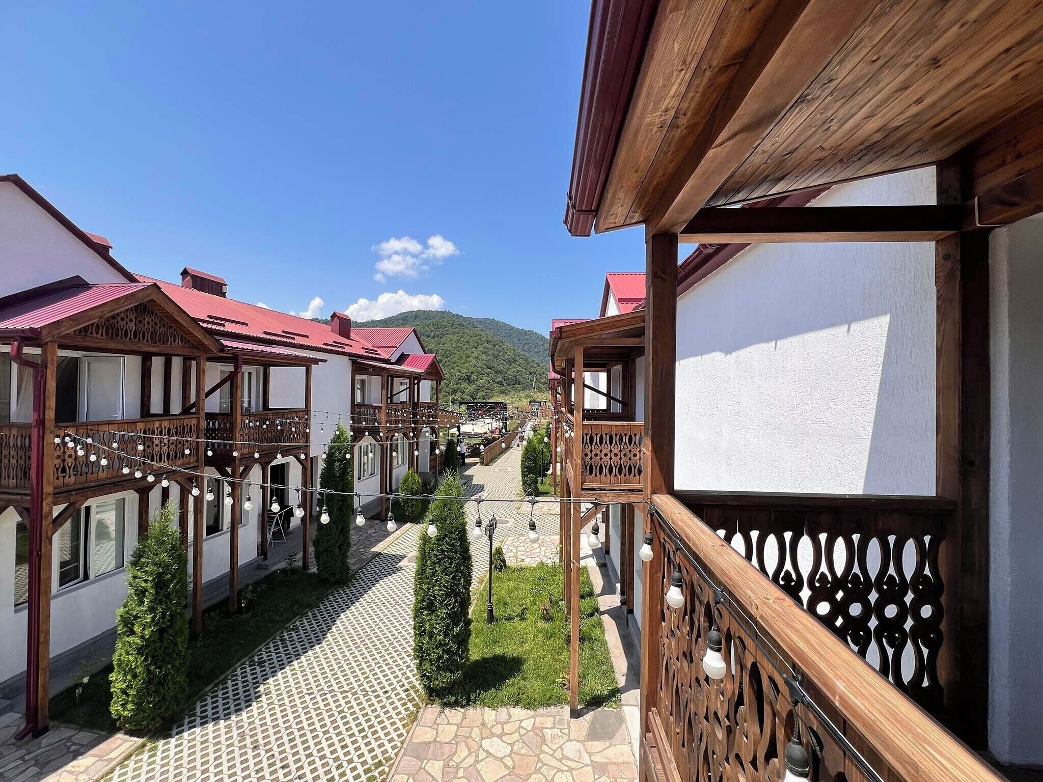 Une rangée de bâtiments traditionnels en bois, dotés de balcons, une cour pavée de pierres et une chaîne de montagnes en arrière-plan.