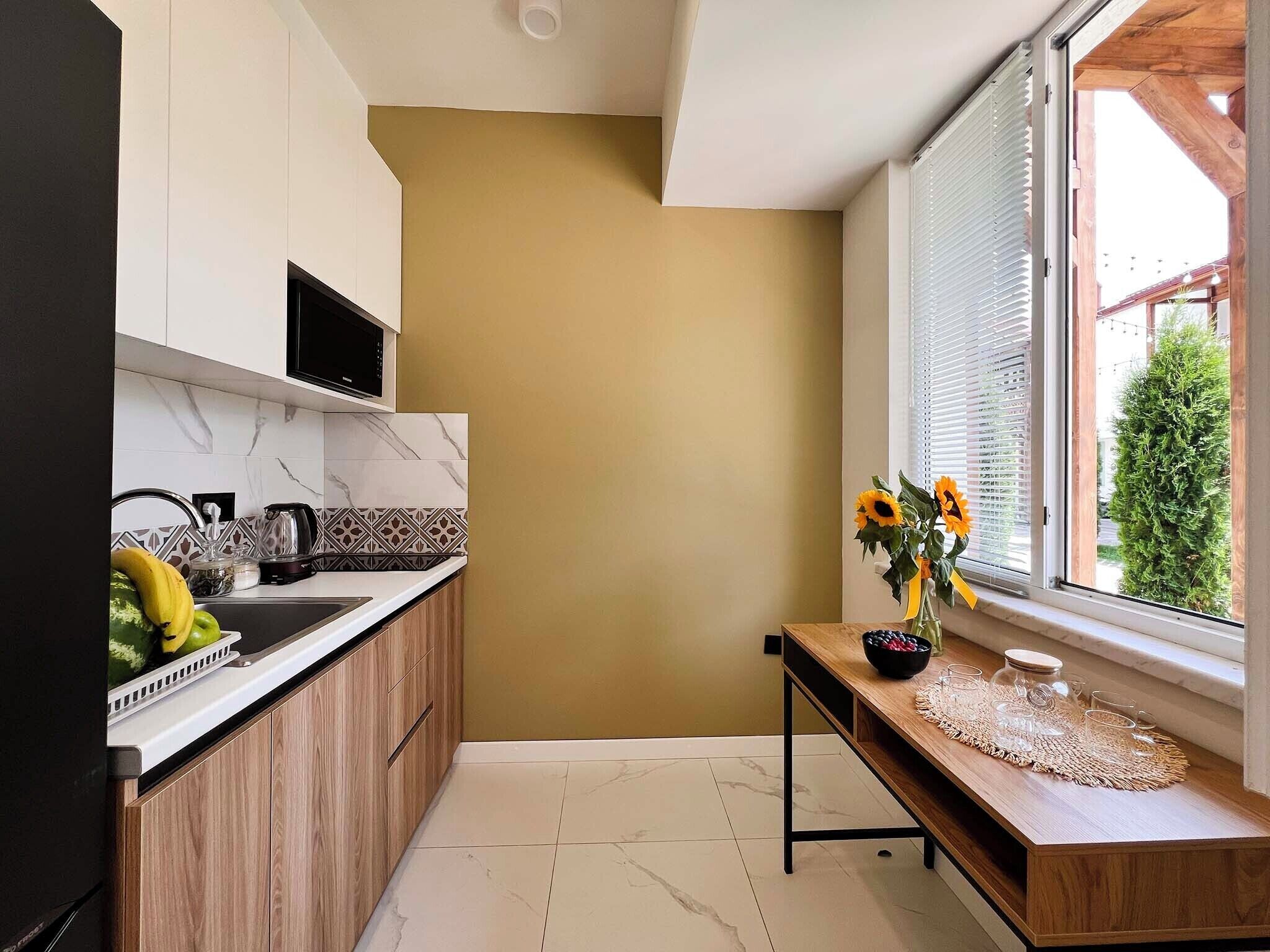 A modern kitchen with a marble backsplash, wooden cabinets, and a window with a view of greenery.