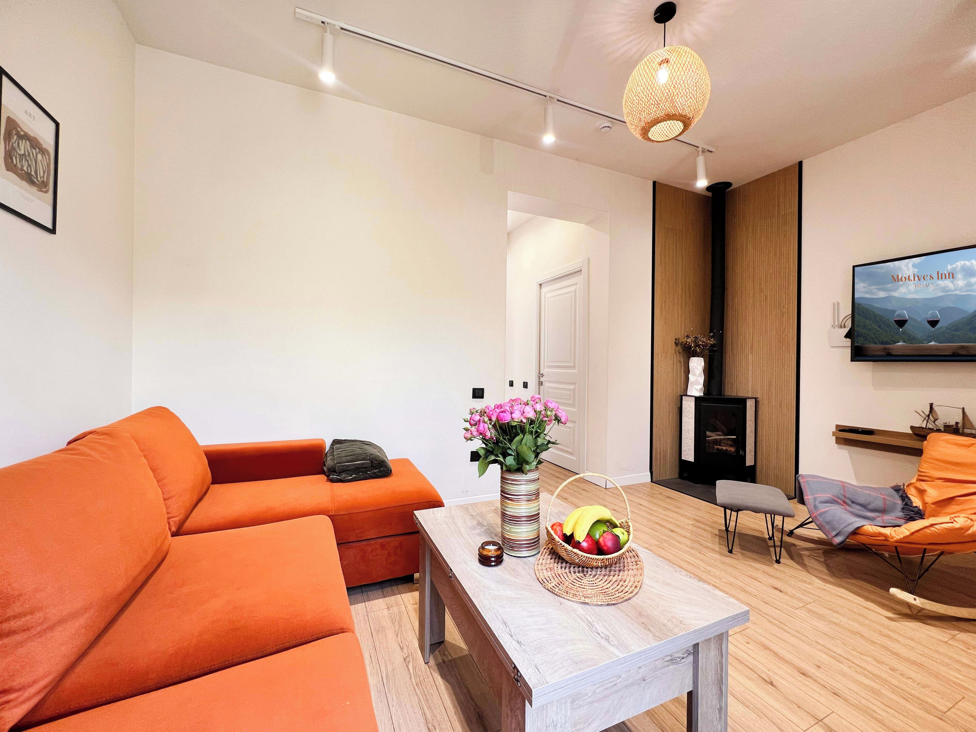 Una sala de estar moderna con un sofá, una mesa de centro con fruta y un televisor que muestra 'Motives Inn'.