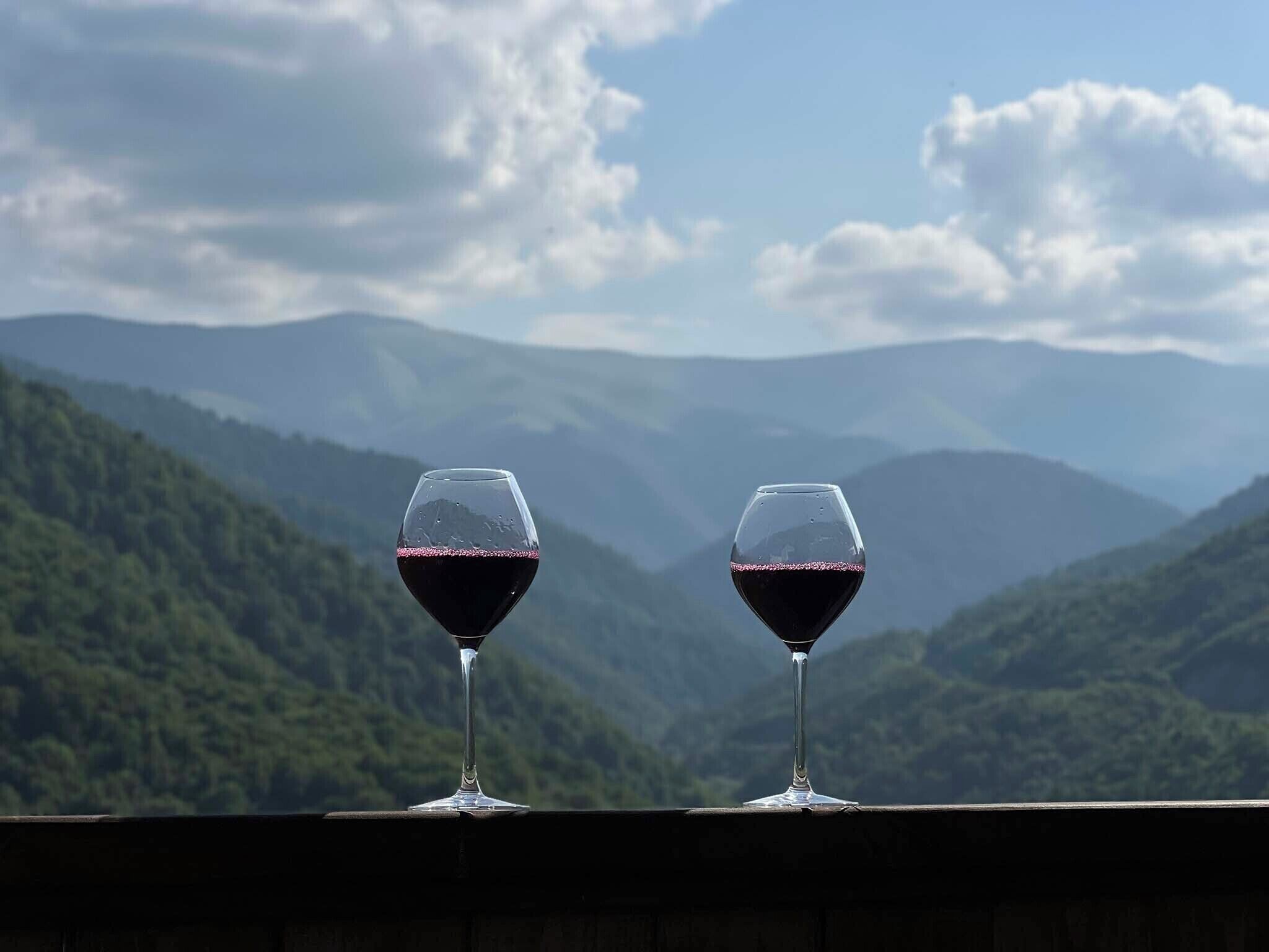 Two wine glasses on a balcony with a mountainous landscape in the background.