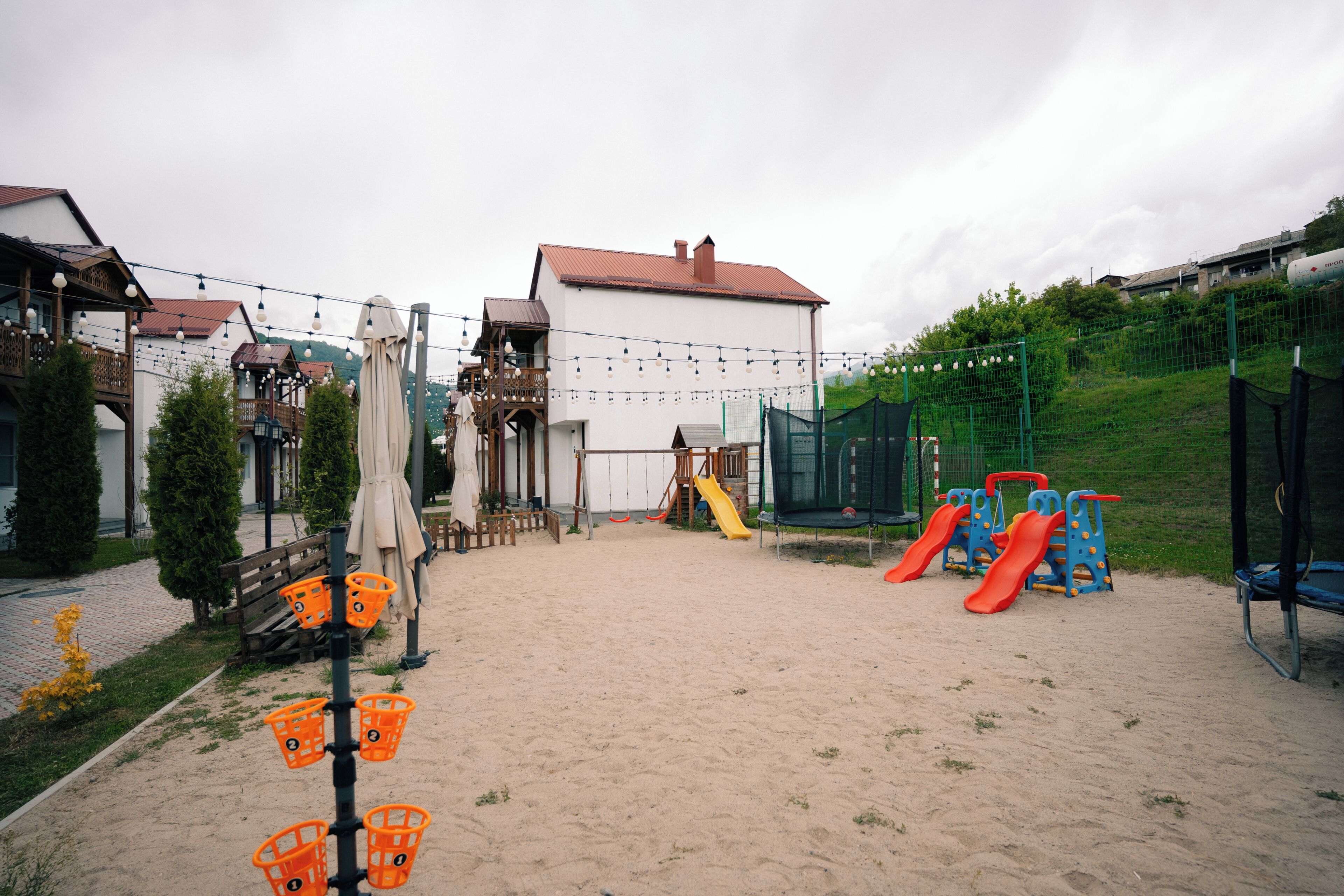 A playground with slides and swings, a white building with a red roof, and a green fence.