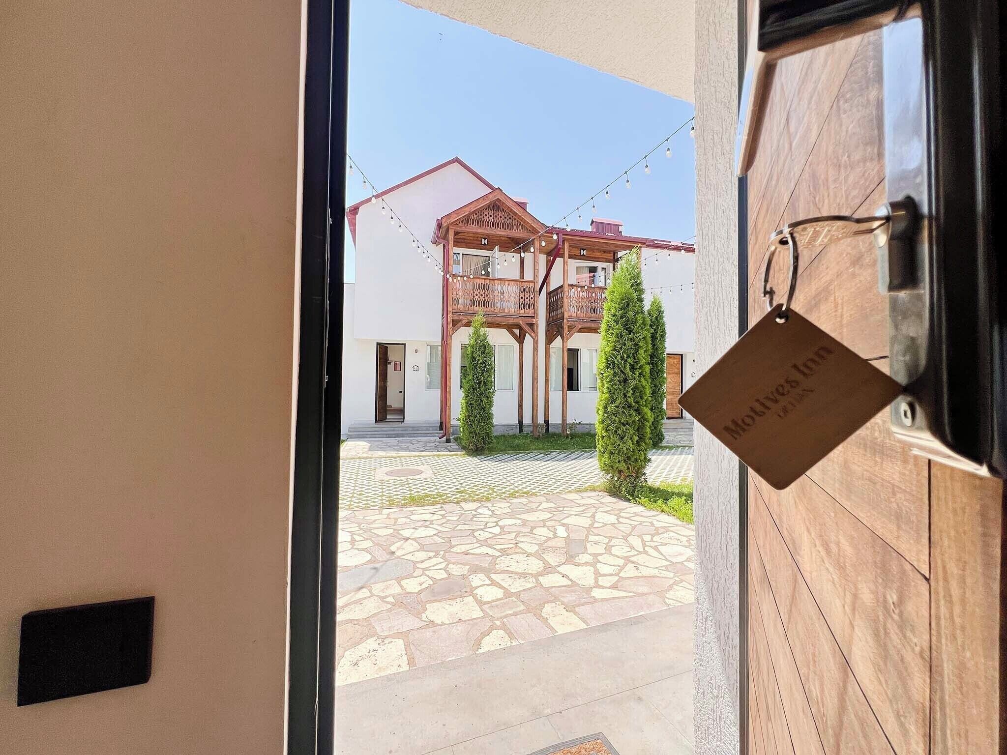 A view through a doorway to a courtyard with a stone-tiled floor, a wooden building with balconies, and a sign hanging on the door.