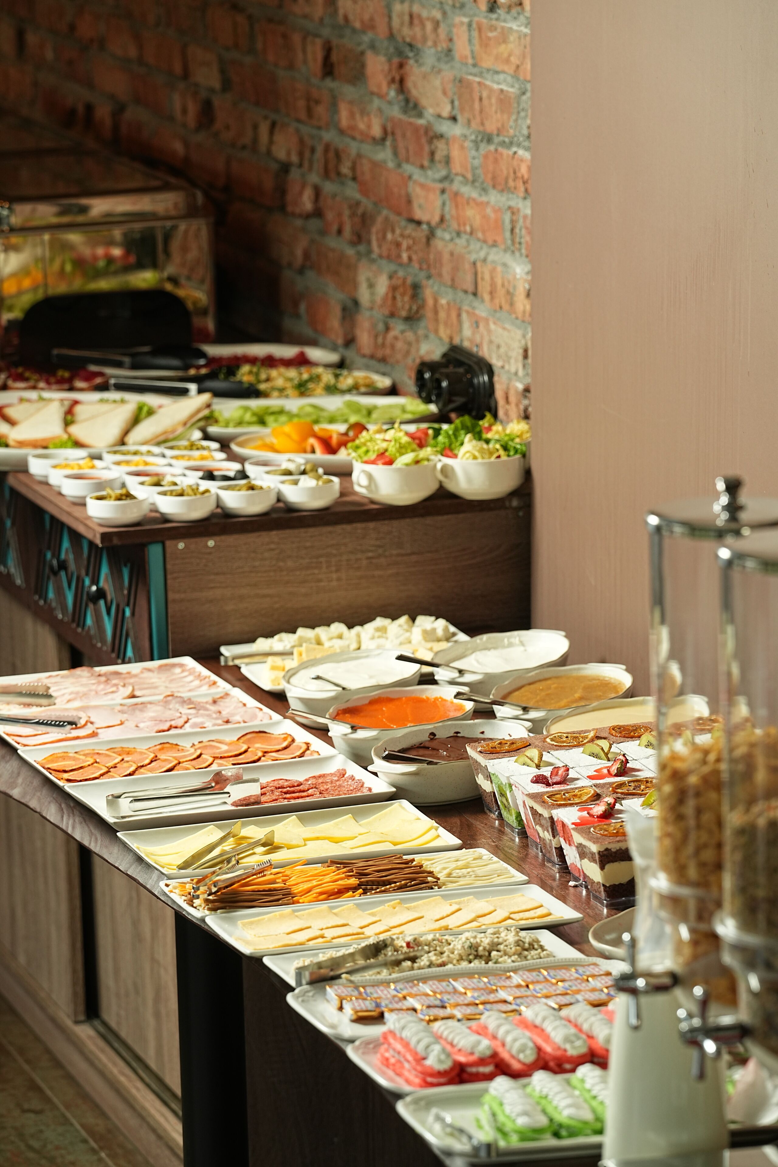 A buffet with various food items and a brick wall in the background.