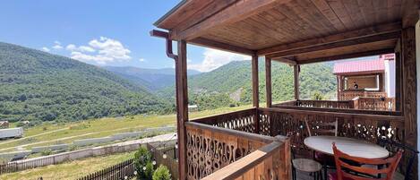 A wooden deck with a table and chairs, overlooking a mountainous landscape.