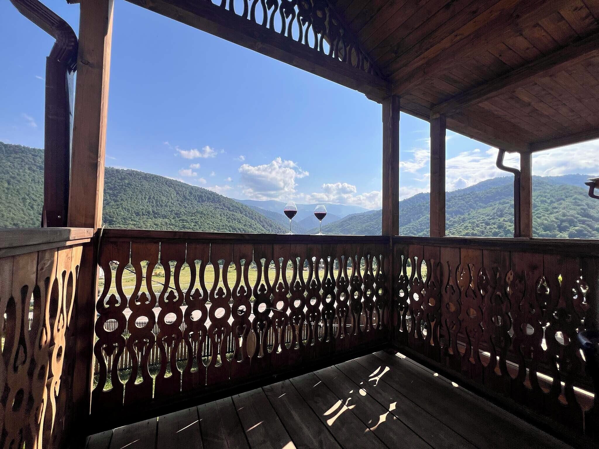 Un balcón de madera con vistas a colinas y montañas verdes.