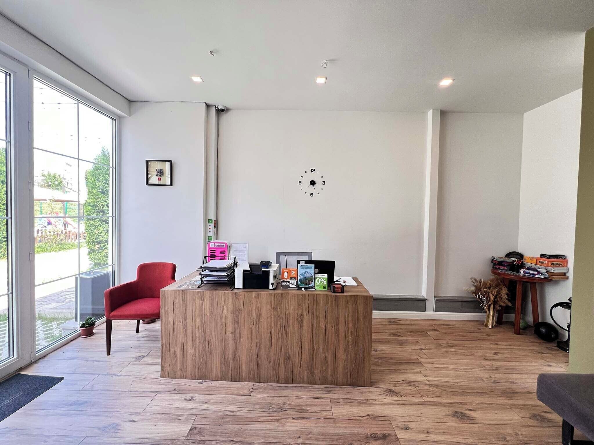 Un espace de bureau moderne avec un comptoir d’accueil en bois, un fauteuil rouge et une grande fenêtre donnant sur l’extérieur.
