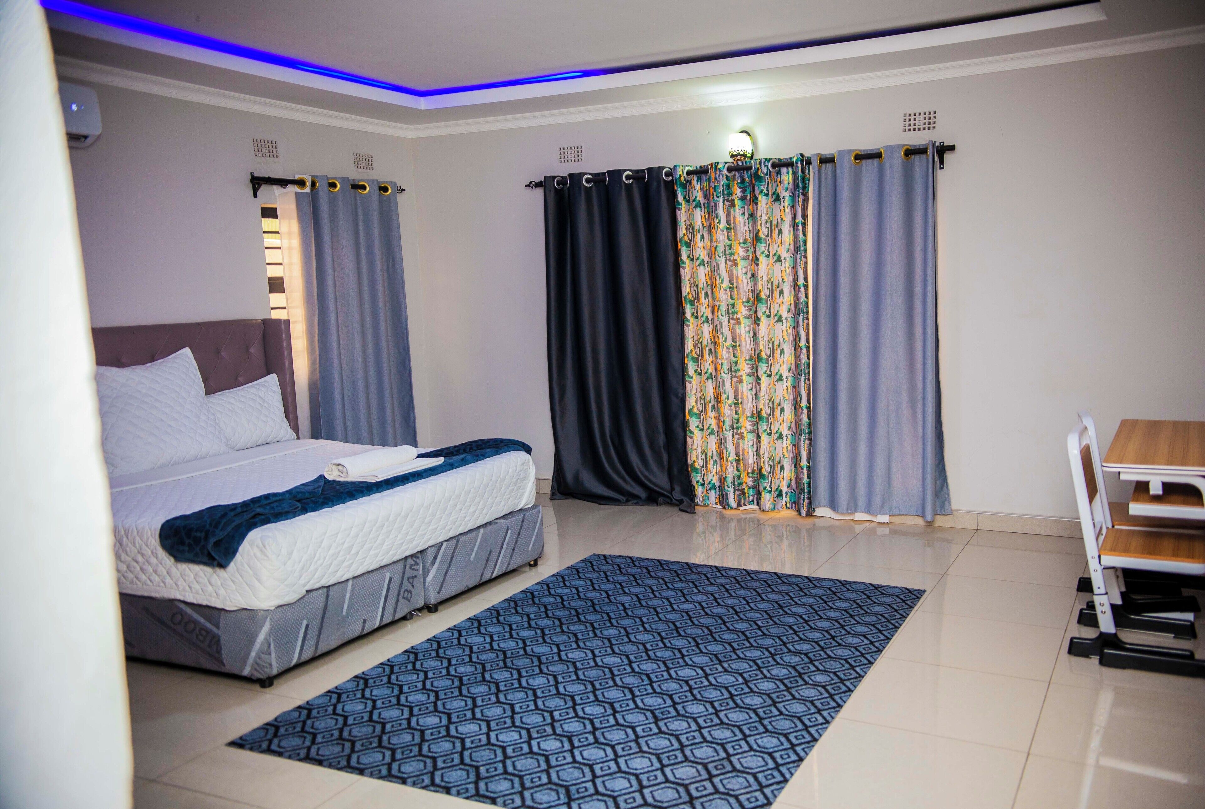 Ein Schlafzimmer mit Bett, Vorhängen, Schreibtisch und einem gemusterten Teppich.