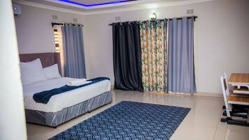 Ein Schlafzimmer mit Bett, Vorhängen, Schreibtisch und einem gemusterten Teppich.
