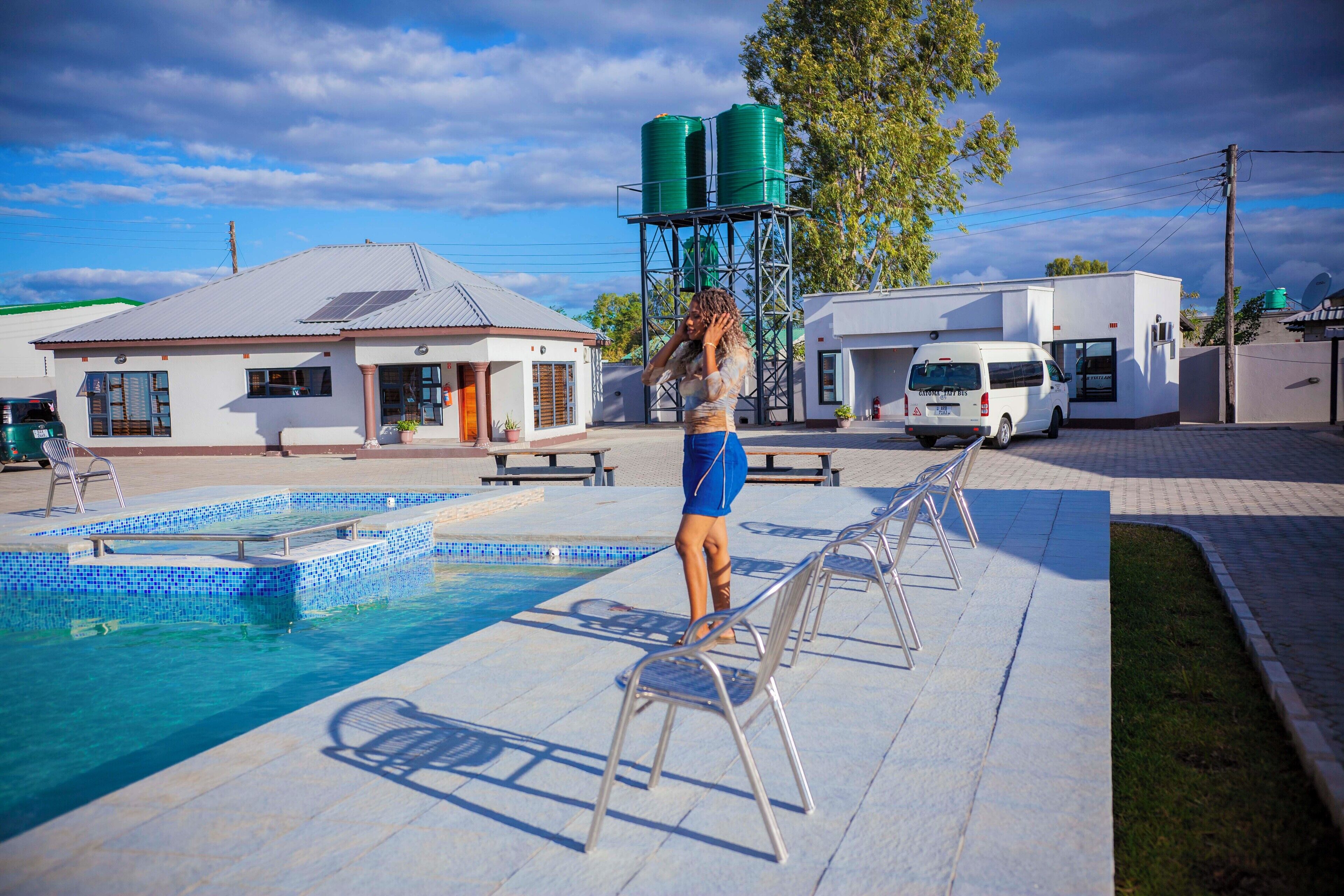 A swimming pool with lounge chairs, a building with a water tower, and a van parked nearby.