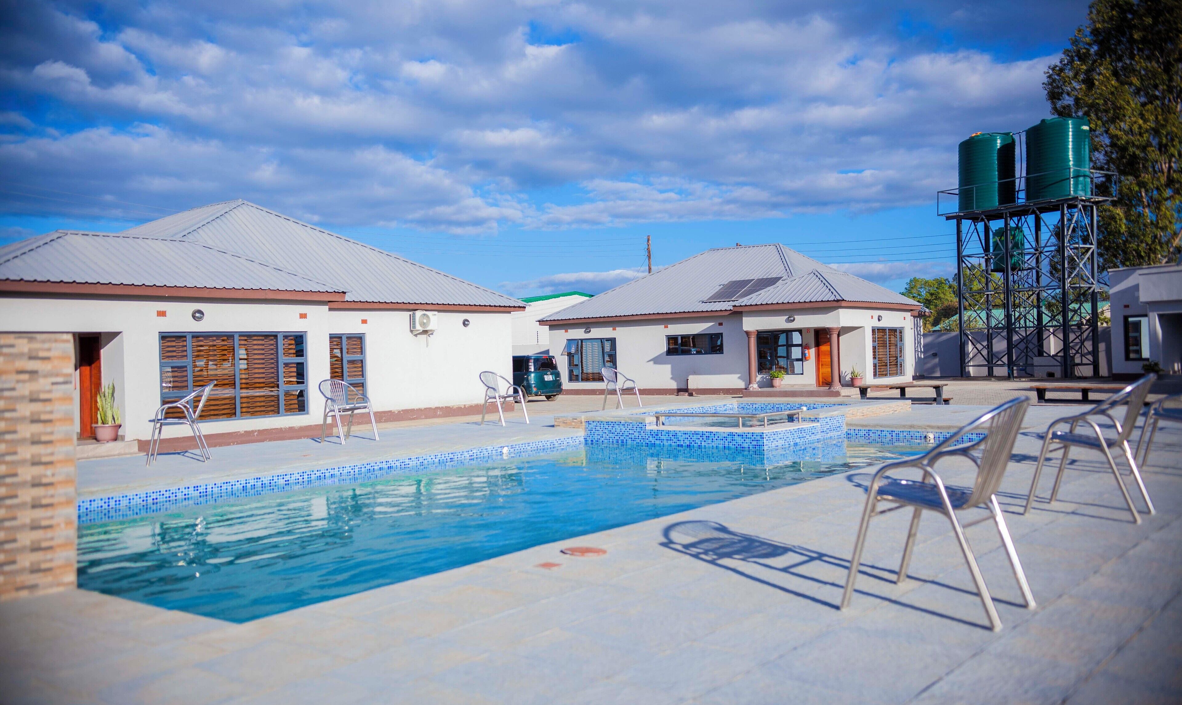 Una piscina con bordes de azulejos, rodeada de edificios con techos metálicos y un tanque elevado de agua.