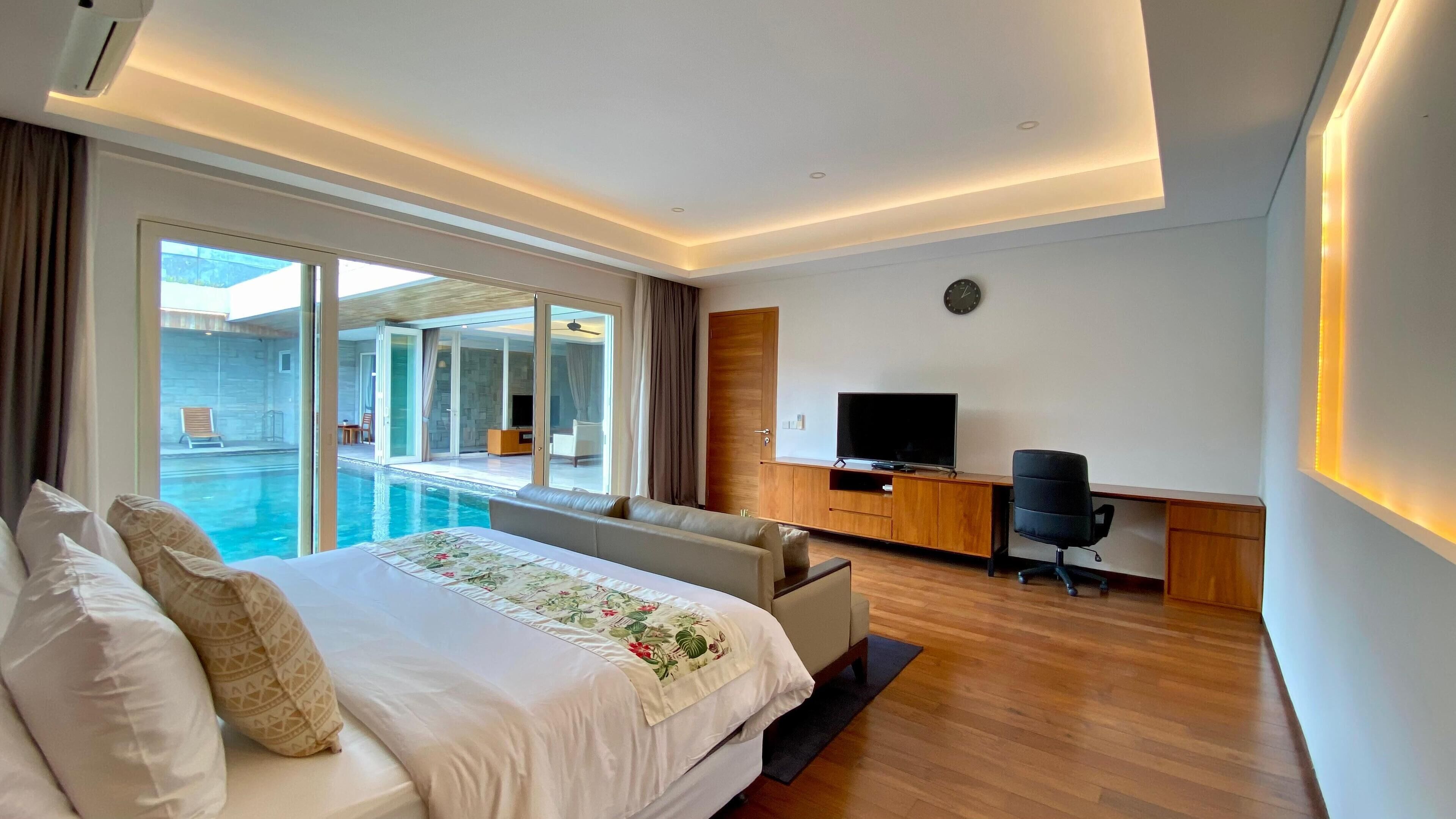 Ein modernes Hotelzimmer mit einem großen Bett, einem Schreibtisch mit Fernseher und Blick auf einen Pool.