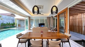 Un comedor moderno con una mesa y sillas de madera, un televisor y vistas a una piscina.