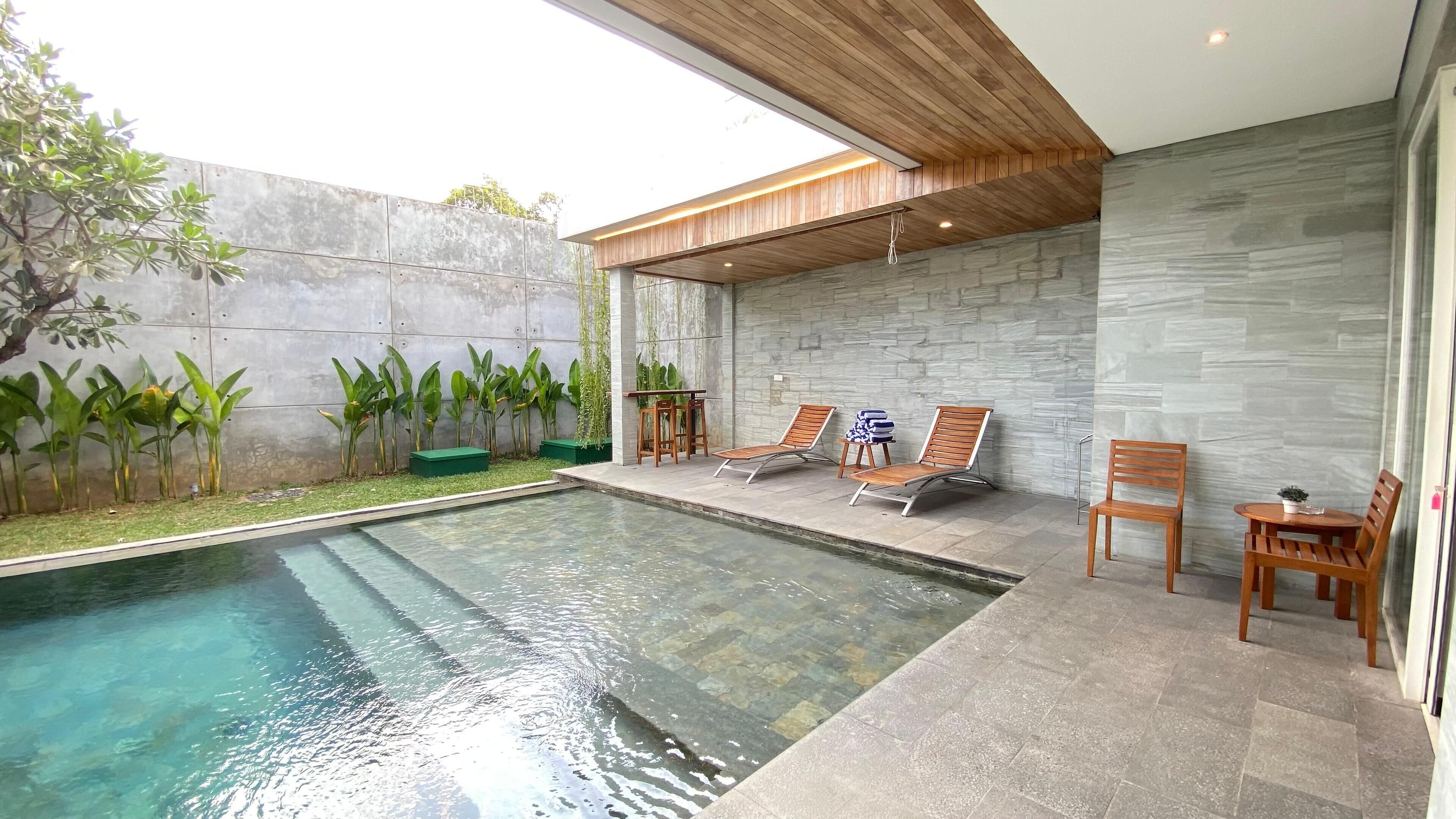 A modern outdoor pool area with clear water, wooden lounge chairs, and a stone wall.