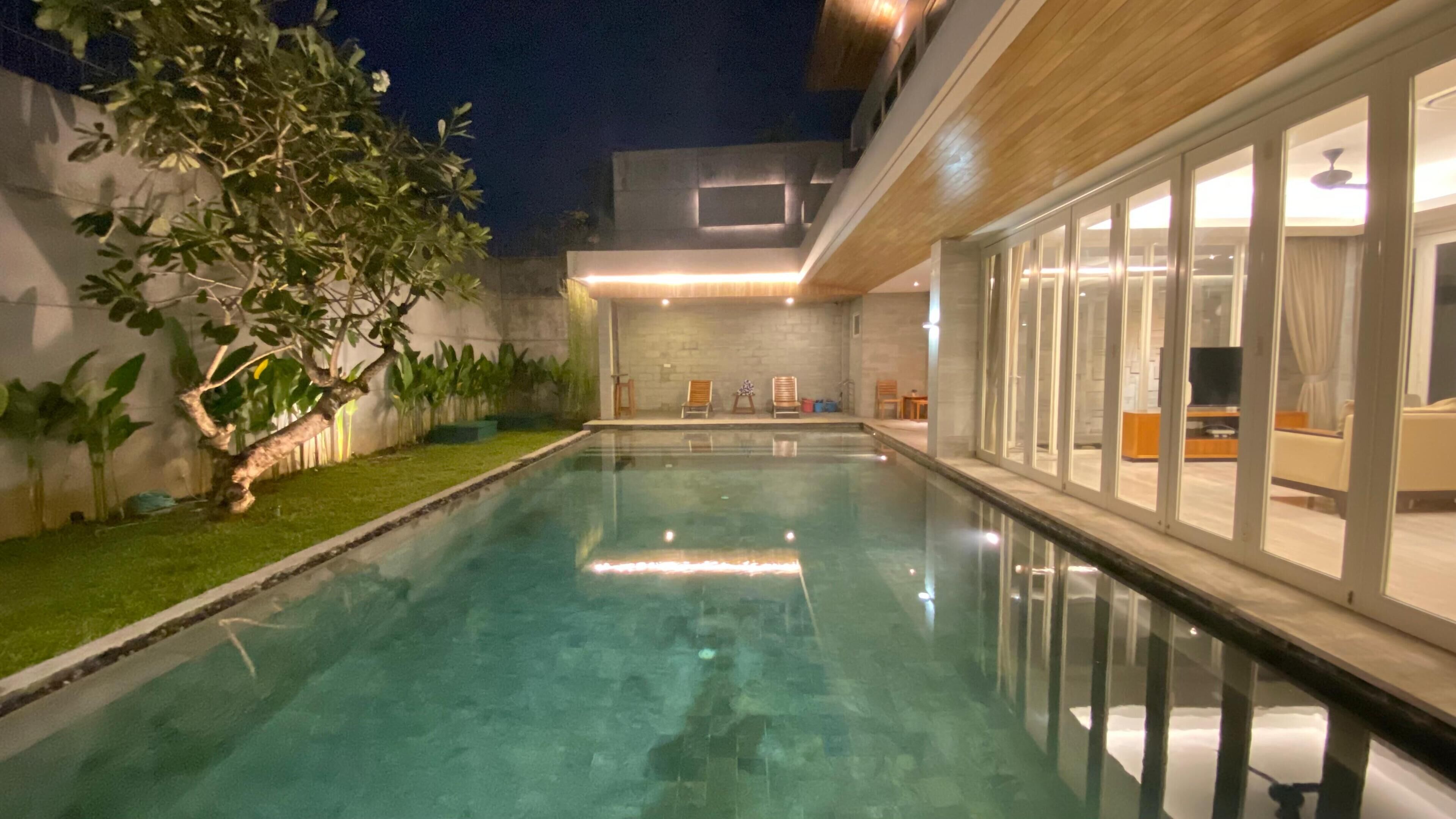 Piscina com vista clara da área circundante, incluindo um gramado bem cuidado e um edifício moderno com grandes janelas.