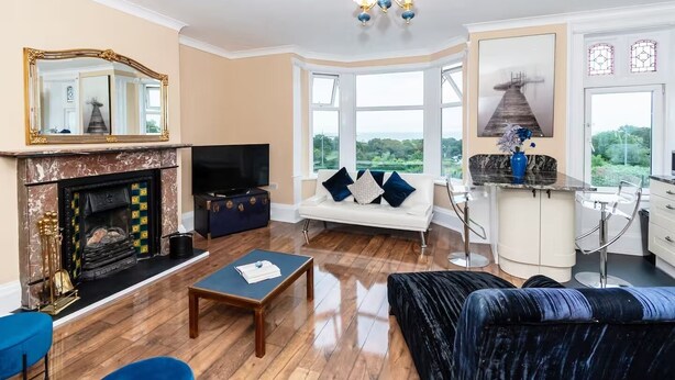 A living room with a fireplace, a television, a sofa, and a view of the outdoors. - Seaview Retreat - Breathtaking coastal views, 2 bedroom apartment (South Shields)