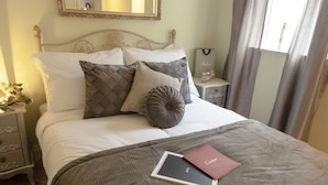A neatly made bed with a grey quilt and pillows, a bedside table with a lamp, and a framed mirror on the wall. - Seaview Retreat - Breathtaking coastal views, 2 bedroom apartment (South Shields)